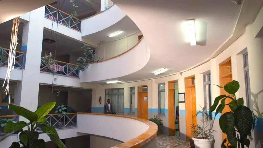 Person walking through hallway with lots of doors in a building with balconies and plants in Ethiopia