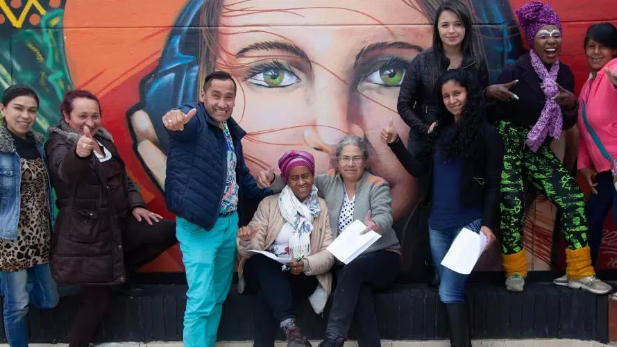 People hold their thumbs up to the camera in front of wall art in Bogota, Colombia