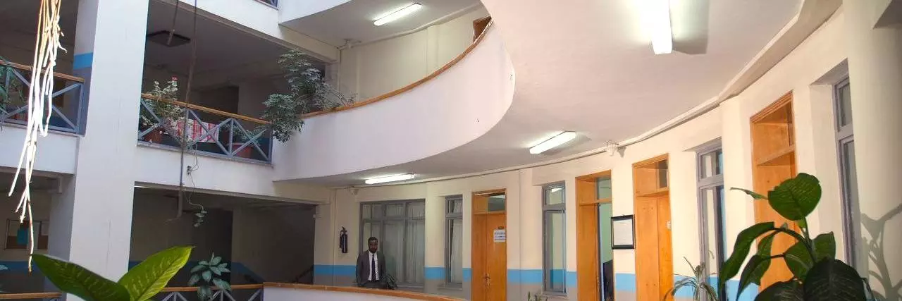 Person walking through hallway with lots of doors in a building with balconies and plants in Ethiopia