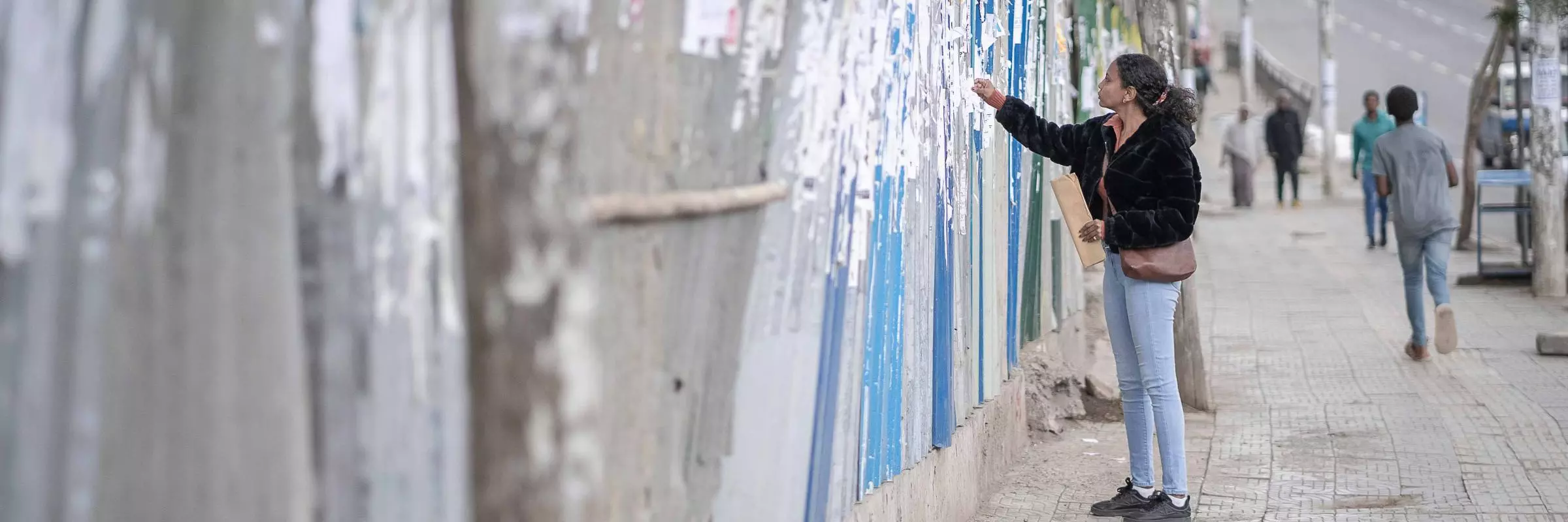 Woman searching through job adverts on a long wall by a road in Ethiopia